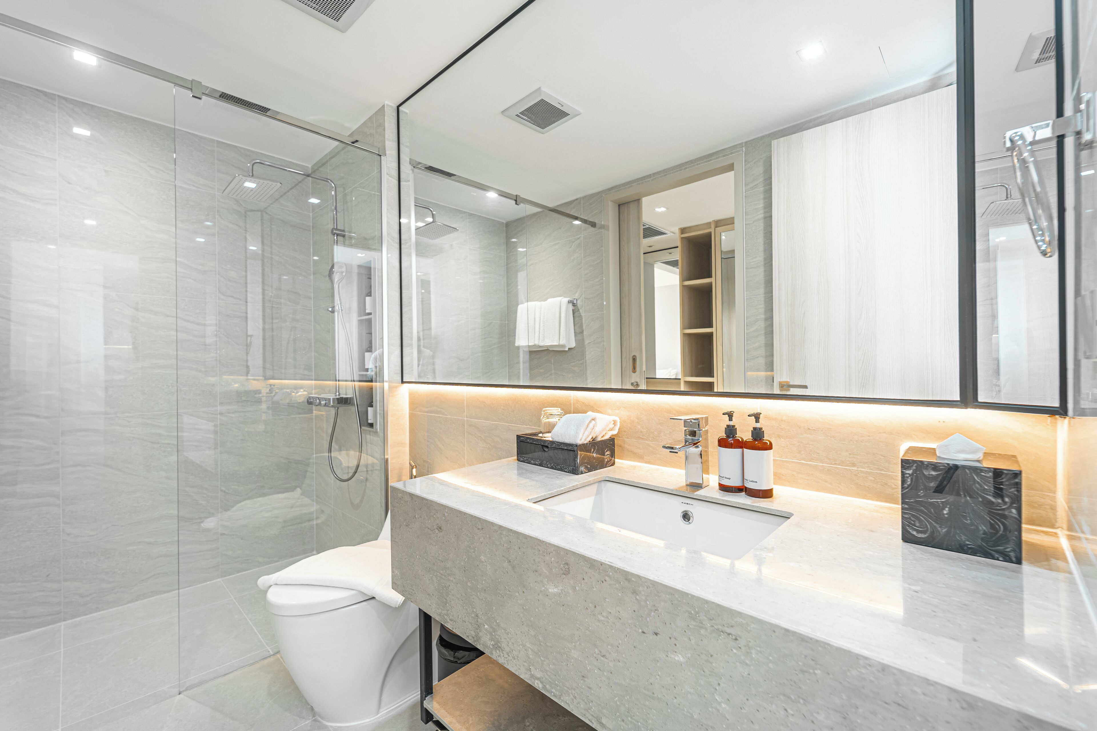 A modern bathroom with a glass-enclosed shower, a white toilet, a marble sink, and a large mirror.