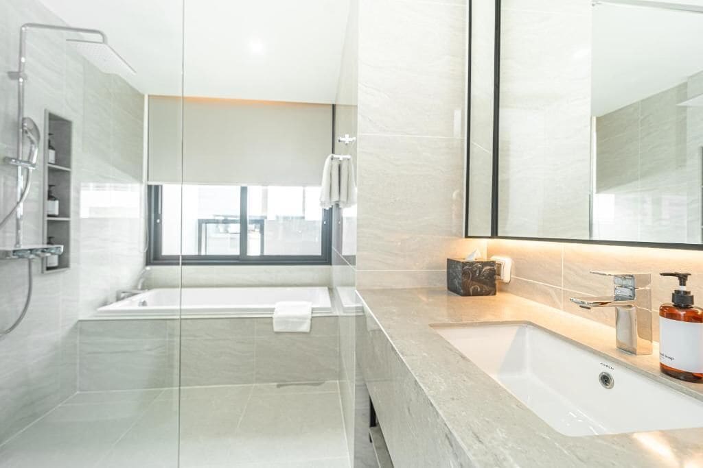 Une salle de bain moderne dotée d’une douche à parois de verre, d’un grand miroir et d’un meuble-lavabo avec un distributeur de savon.