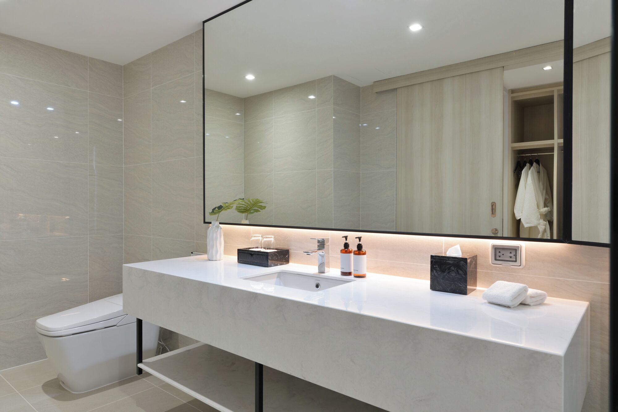 A modern bathroom with a large mirror, two sinks, a toilet, and a towel rack.