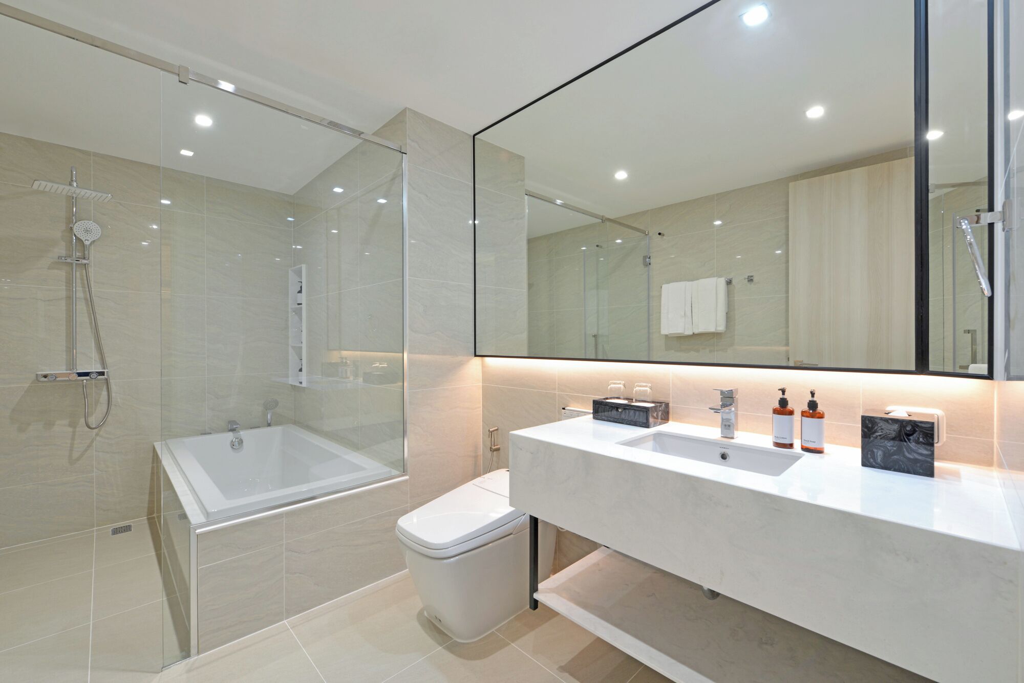 A modern bathroom with a glass-enclosed shower, a white bathtub, and a vanity with two sinks and a mirror.