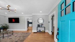 A modern living room with a flat-screen TV, a round mirror, and a blue door.