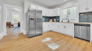 A modern kitchen with white cabinets, a stainless steel refrigerator, a dishwasher, and a blue tiled backsplash.