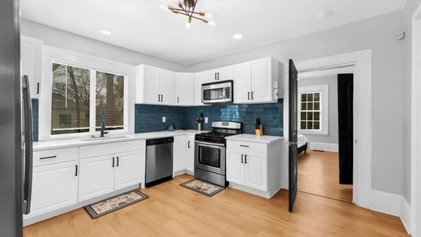 A modern kitchen with white cabinets, a stainless steel refrigerator, a microwave, and a stove.