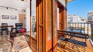 A balcony with a wooden door, a dining table with chairs, a rug, and a view of buildings. - Solaga - Mary (Málaga)