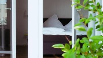 A bedroom with a bed, a window, and a view of another room.