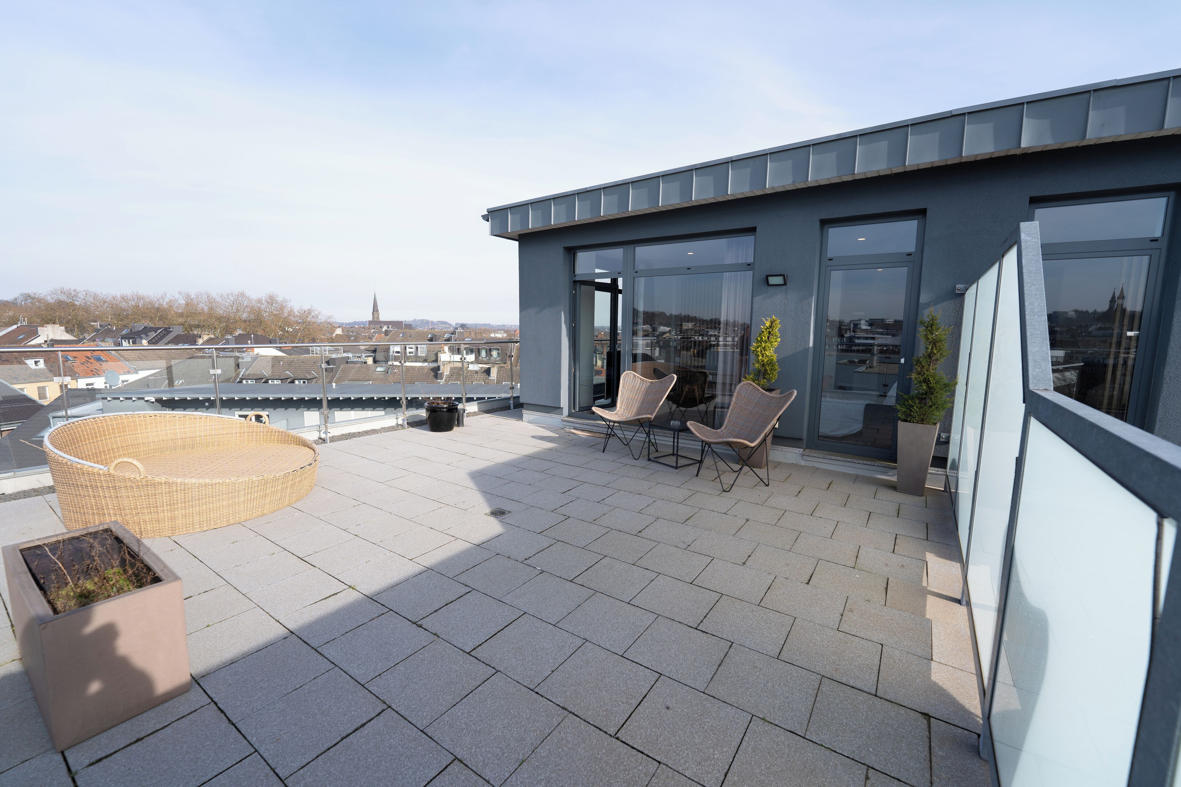 A rooftop terrace with a seating area, a large wicker chair, and a planter.