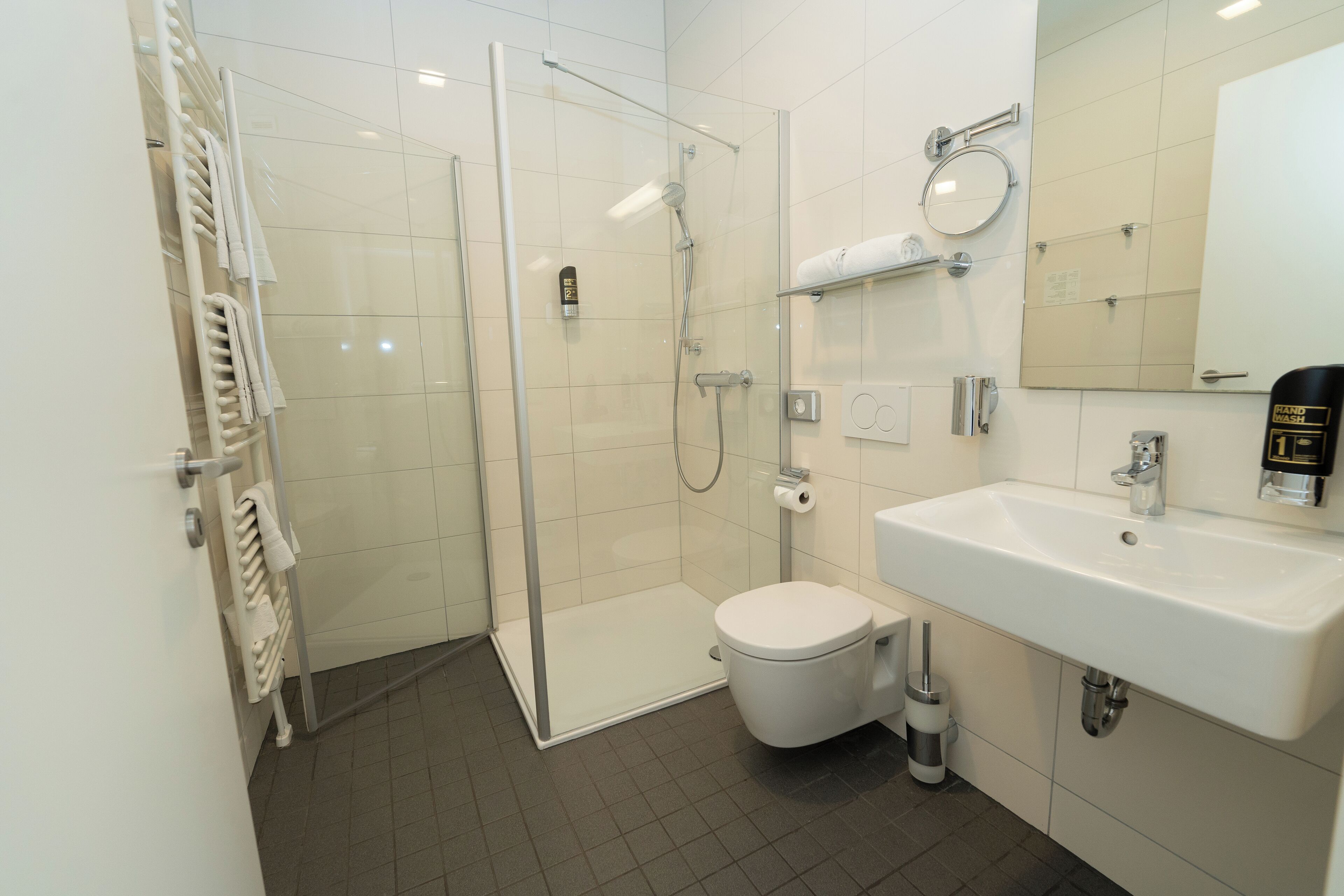 Une salle de bain moderne avec une douche à parois de verre, des toilettes blanches et un lavabo surmonté d’un miroir.