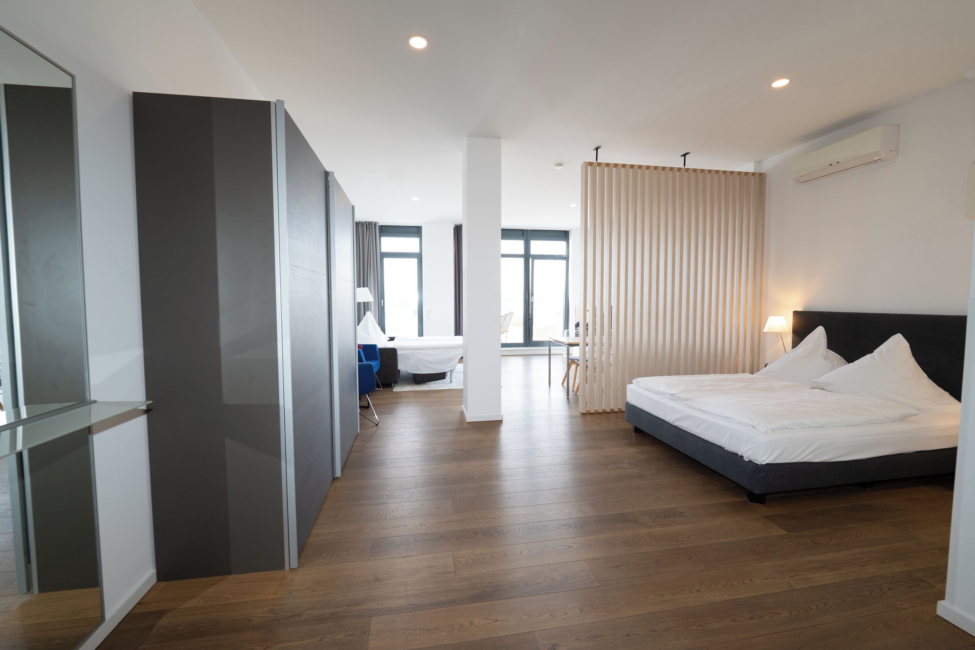 Een moderne hotelkamer met een groot bed, een bureau en een stoel. Er is een raam met gordijnen, een plafondlamp en een airconditioner.