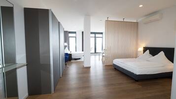 Een moderne hotelkamer met een groot bed, een bureau en een stoel. Er is een raam met gordijnen, een plafondlamp en een airconditioner.