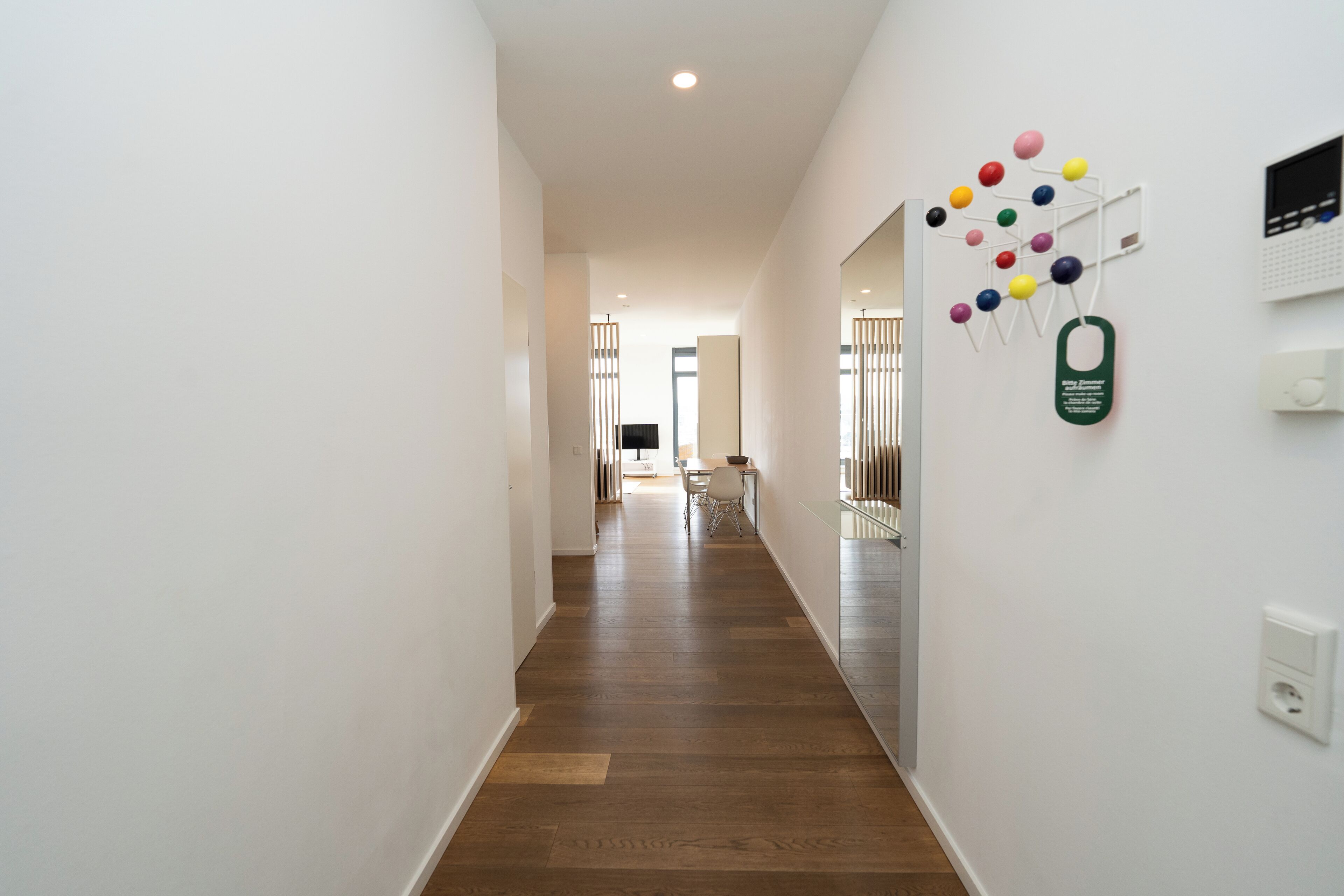 Un couloir doté d’un plancher en bois, de murs blancs et d’un coin repas situé au fond.