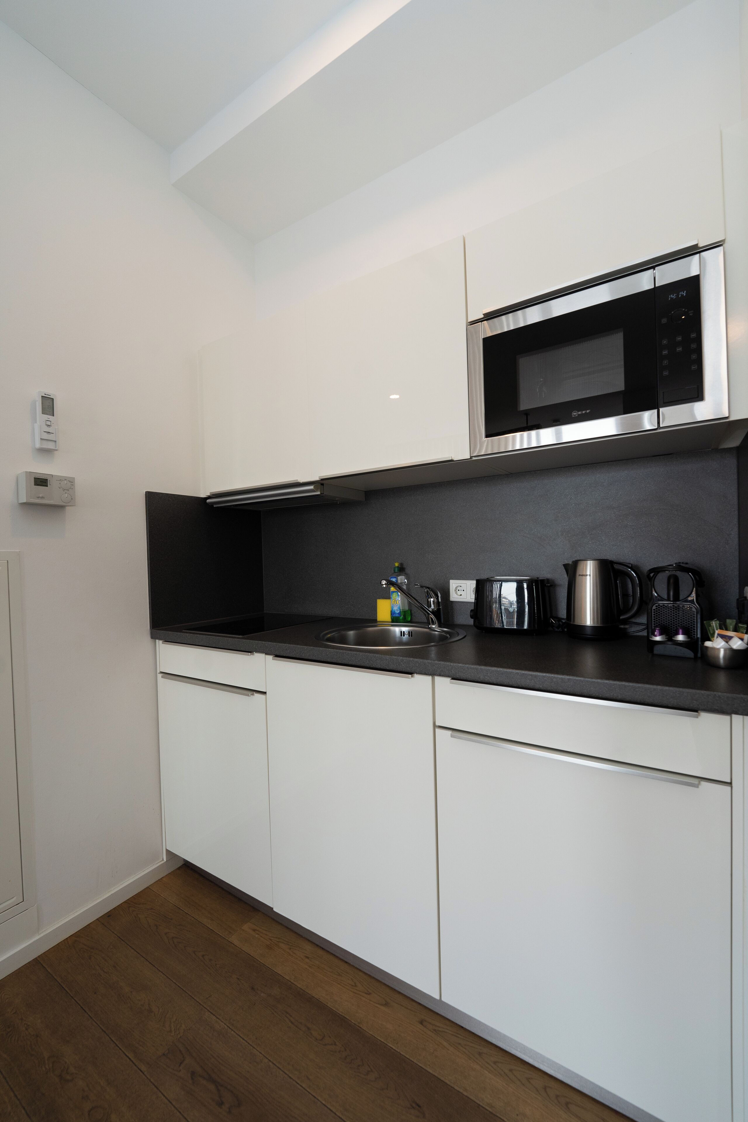 Una cocina moderna con armarios blancos, un microondas de acero inoxidable, una tetera y una cafetera sobre la encimera.