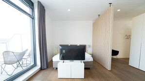 A modern bedroom with a large window, a bed, a TV, and a seating area by the window. - Das Loft Apartments (Aachen)