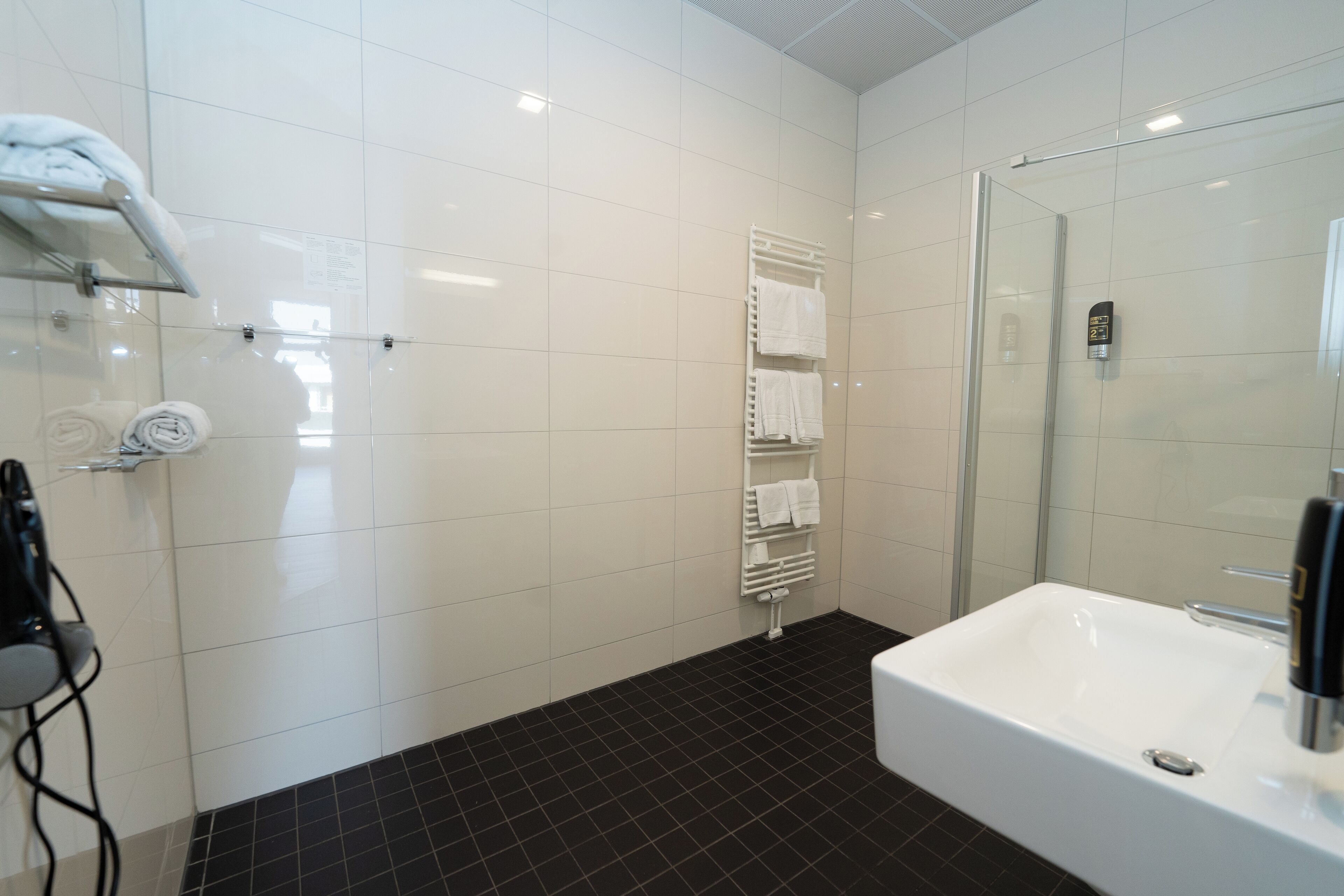 A modern bathroom with a white bathtub, a glass shower enclosure, and a towel rack with neatly folded towels.