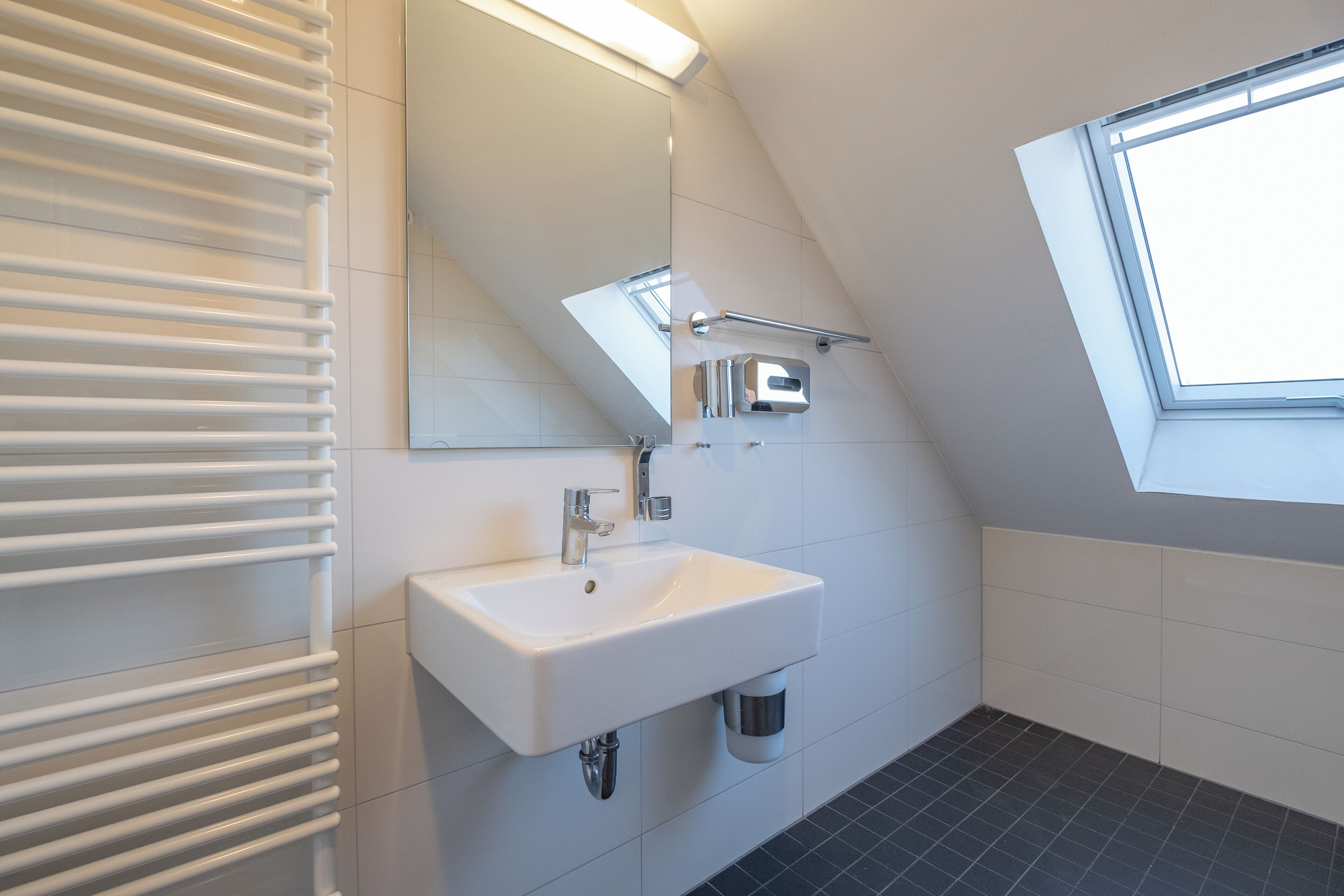 A modern bathroom with a white sink, a mirror, and a window.