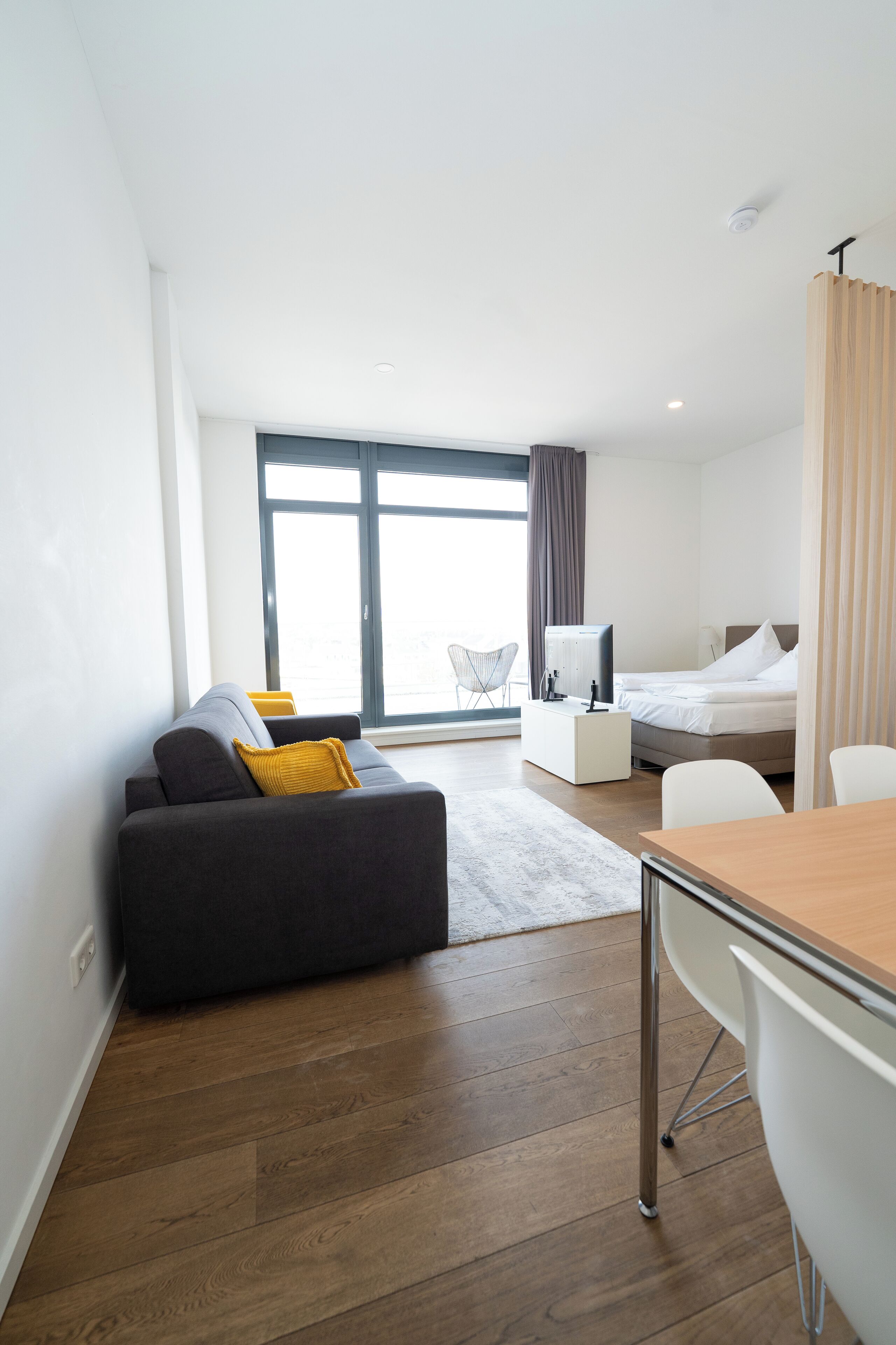 A modern hotel room with a sofa, a bed, a desk, and a chair.