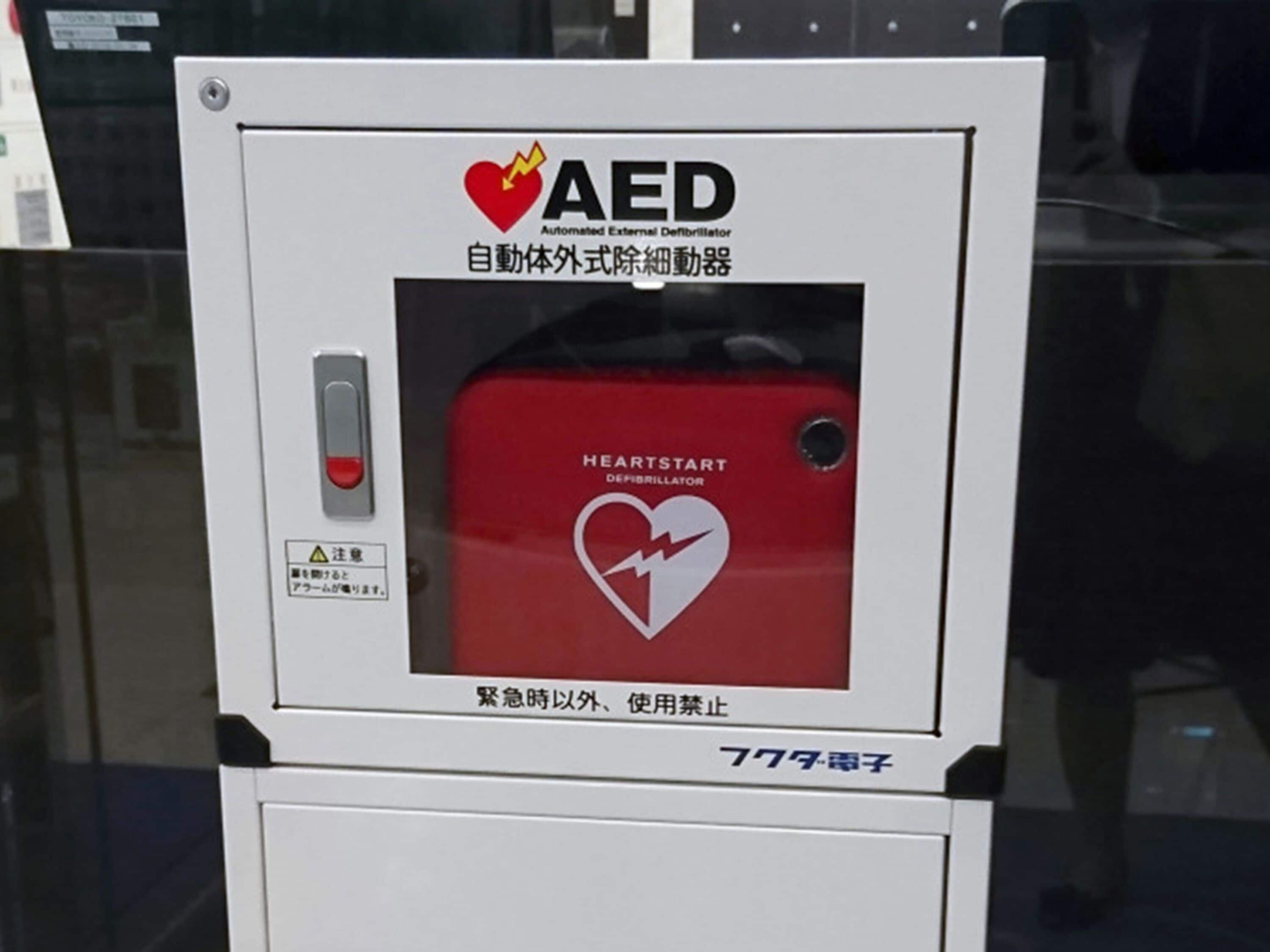 An AED device with a red and white design, labeled "HEARTSTART" and "AED" for automated external defibrillation.
