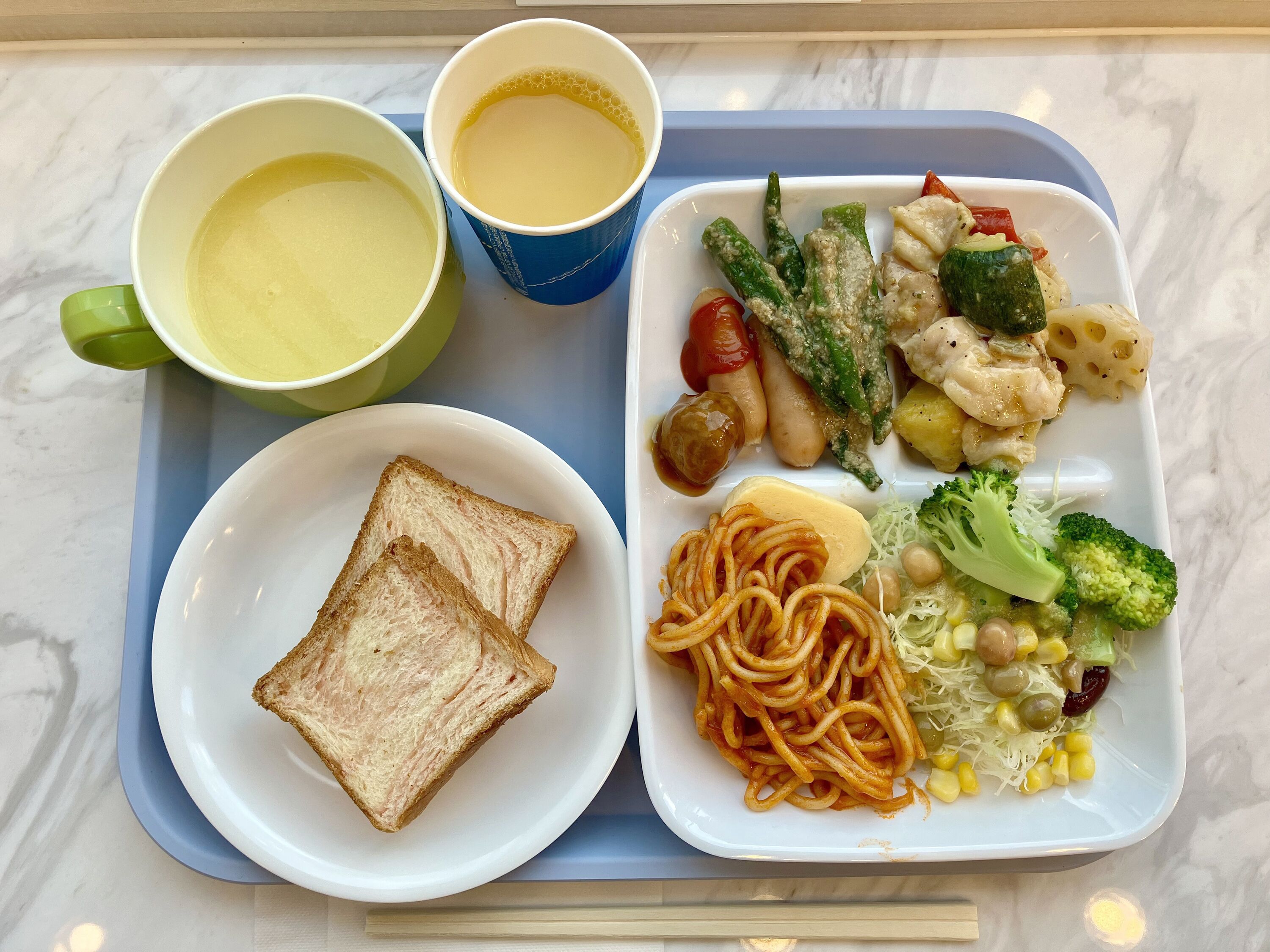 Una bandeja con espagueti, pan, dos tazones de sopa y una variedad de verduras.