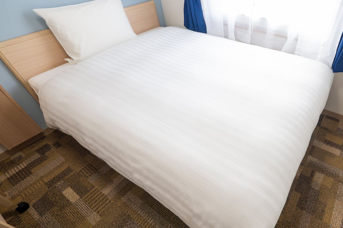 Un lit bien fait, avec une literie blanche, une tête de lit en bois et un tapis à motifs.