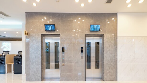 Een modern liftgedeelte met twee liften, een receptiebalie en een digitaal scherm boven de liften.