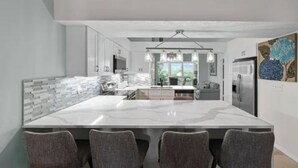 A modern kitchen with a large island, white cabinetry, and a chandelier. - 2 Bed + Den condo in charming Naples with, private pool, WiFi. Relax and unwind (Naples)