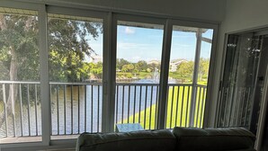 A balcony with a view of a lake, a grassy area, and buildings in the distance. - 2 Bed + Den condo in charming Naples with, private pool, WiFi. Relax and unwind (Naples)