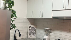 Ett kök med vita skåp, en bänkskiva i granit, en diskho, en mixer och en spis.