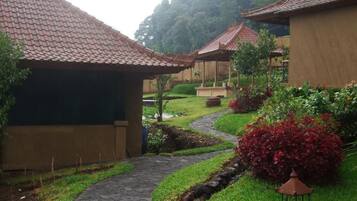 A pathway leading to traditional-style buildings with tiled roofs, surrounded by lush greenery and a small water feature.