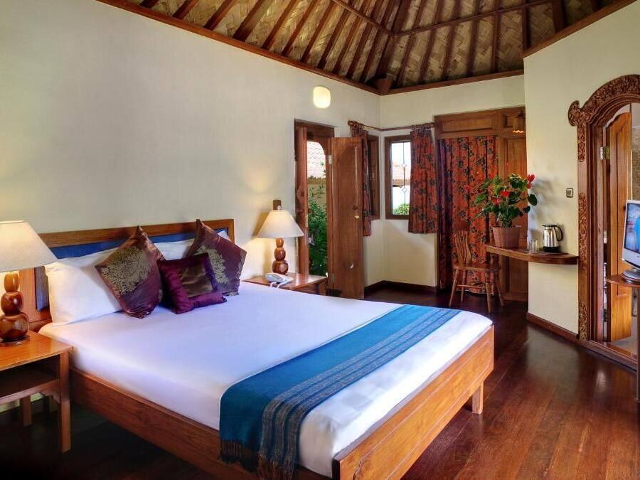 Un dormitorio ordenado con una cama de madera, dos mesitas de noche con lámparas, un televisor y un escritorio con una silla.