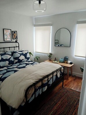 Une chambre à coucher avec un lit, un bureau, un miroir et deux fenêtres.