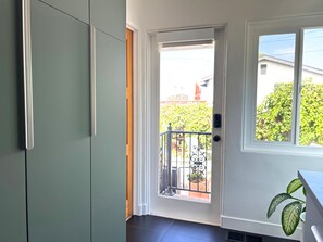 A room with a sliding door leading to an outdoor balcony, a window with a view of greenery, and a potted plant on the windowsill.