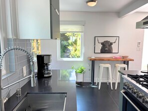 Una cocina moderna con estufa a gas, cafetera y ventana con vista a zonas verdes.