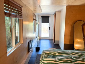 A hallway with wooden walls, a bed with a zebra print bedspread, and a door leading to a bright room. - Golden Hour House OB (San Diego)