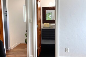 Ein Korridor mit einer Holztür, einer weißen Wand, einem Fenster mit Jalousien und einer kleinen Pflanze.