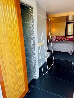 Une chambre à coucher moderne avec un lit, une étagère en métal blanc, un mur en pierre et une porte en bois.