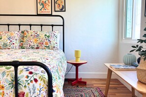 Un dormitorio con cama, una mesita, una lámpara y una ventana.