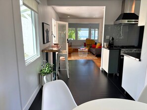 A modern kitchen with a stove, a dining area with a white table, and a living room with a sofa and a coffee table. - Golden Hour House OB (San Diego)