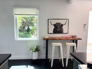 A modern kitchen with a window, a plant, a bull-themed artwork, and bar stools.