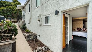 A modern house with a narrow driveway, a stone garden bed, and a bedroom with a dark floor. - Zen Point Loma Garden House (San Diego)