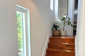 Eine Treppe mit Holzbodenstufen führt zu einer Zwischenebene, begrenzt von weißen Wänden und einem Fenster.