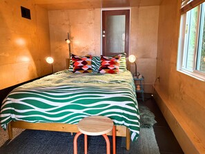 A bedroom with a bed, pillows, a nightstand, a lamp, and a window.
