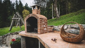 A brick outdoor oven with a chimney, a stone bench, and a woven basket on a tiled patio. - Gorenja Trebuša, Domačija Gačnik (Tolmin)