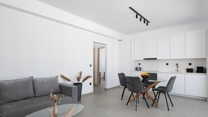 Ett modernt vardagsrum med ett soffbord i glas, en grå soffa och en matplats med stolar och ett bord.