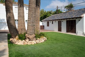 A courtyard with a well-maintained lawn, palm trees, and a white building with a tiled roof. - La moderna suites (Málaga)