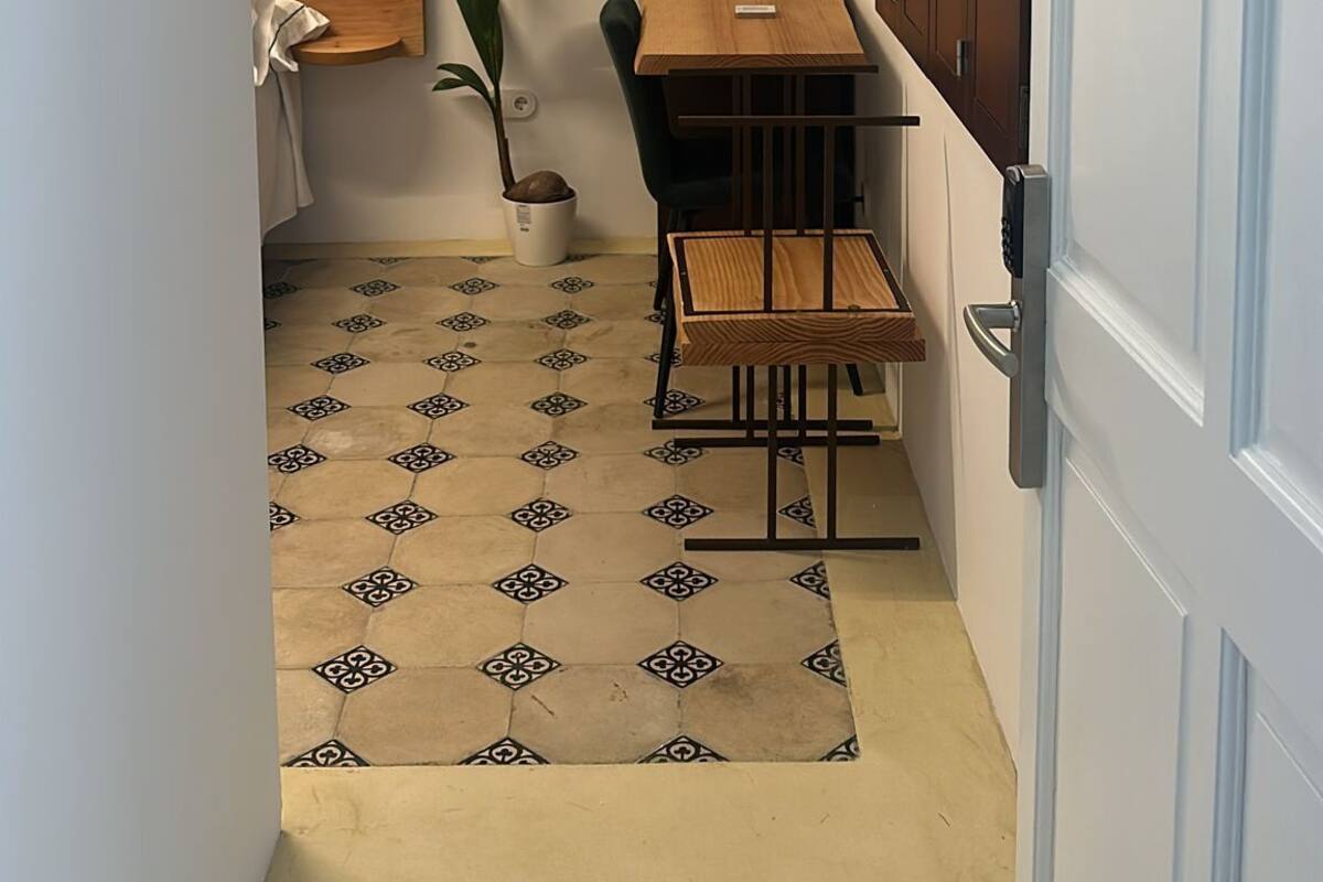 A small, narrow room with a wooden desk, a chair, a lamp, a potted plant, and a cabinet with a towel hanging on the door.
