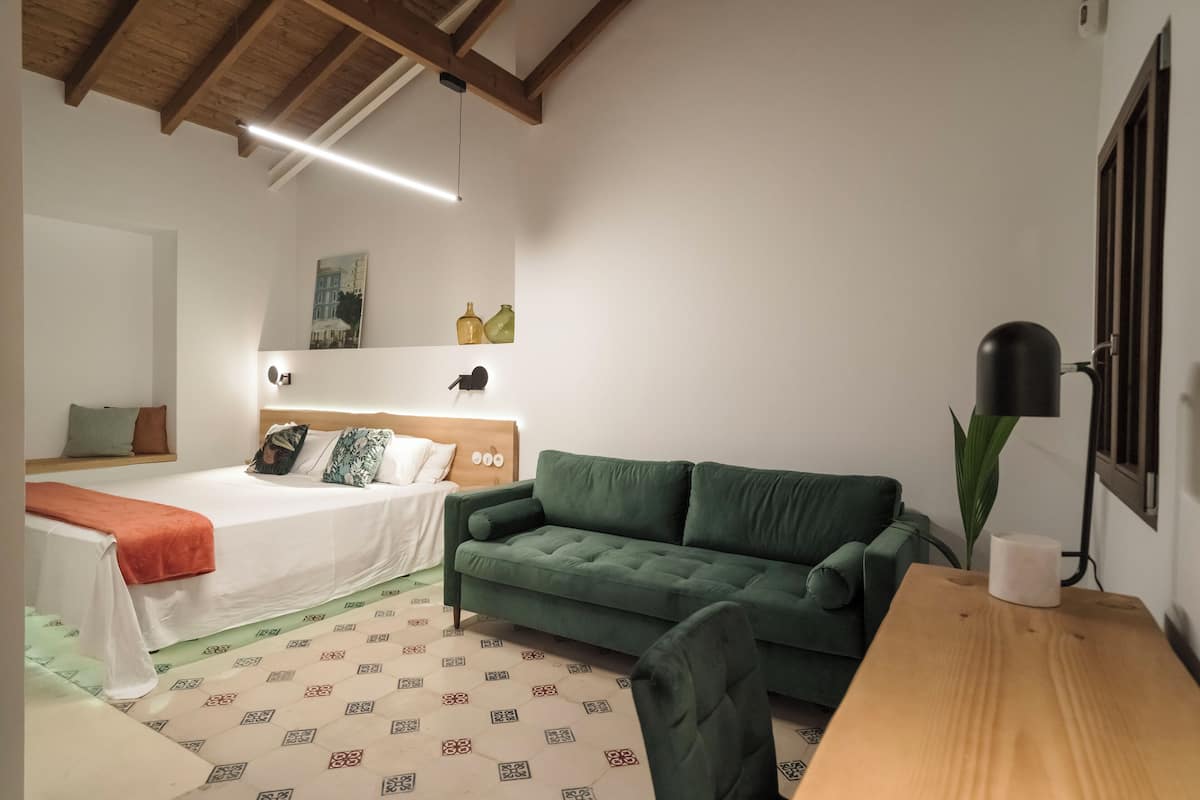 A bedroom with a bed, a green sofa, a wooden table, and a lamp.