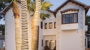 A modern two-story house with a well-maintained lawn and three illuminated palm trees. - La moderna suites (Málaga)