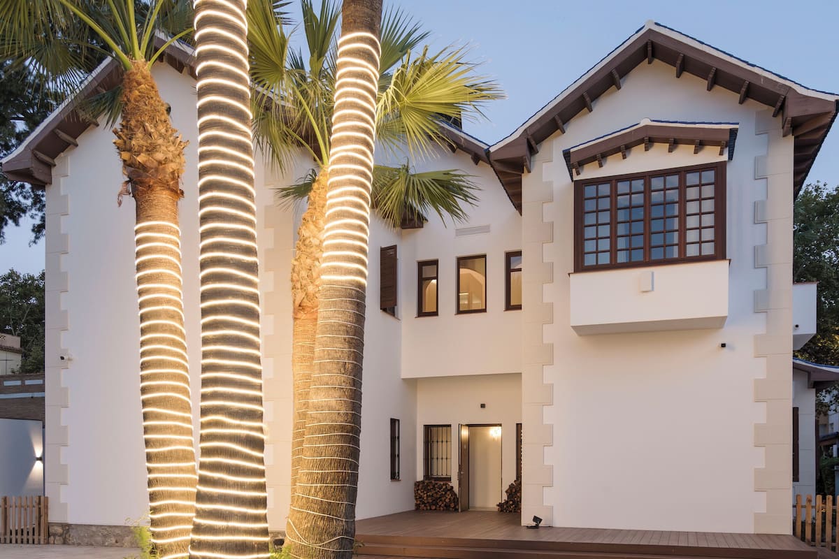 A modern two-story house with a well-maintained lawn and three illuminated palm trees.