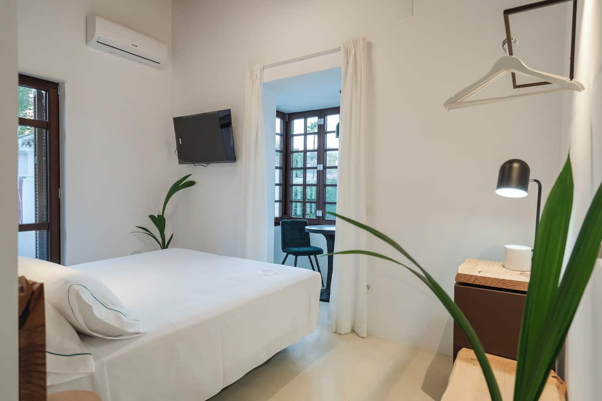 A bedroom with a bed, a desk, a chair, a TV, and a hanging light fixture.