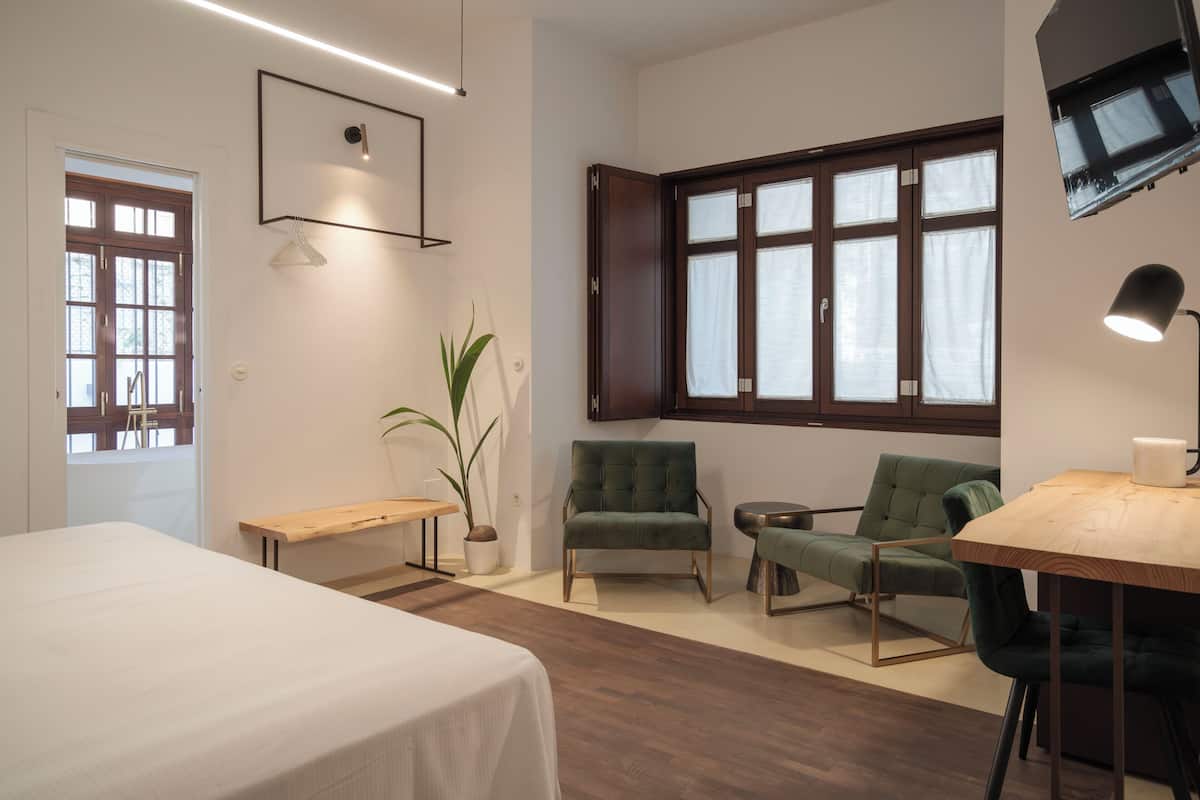 A modern room with a bed, two chairs, a small table, a potted plant, and a window with curtains.
