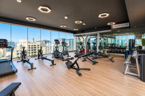 Un gimnasio moderno con equipo de ejercicio variado, ventanas amplias y vista a la ciudad.